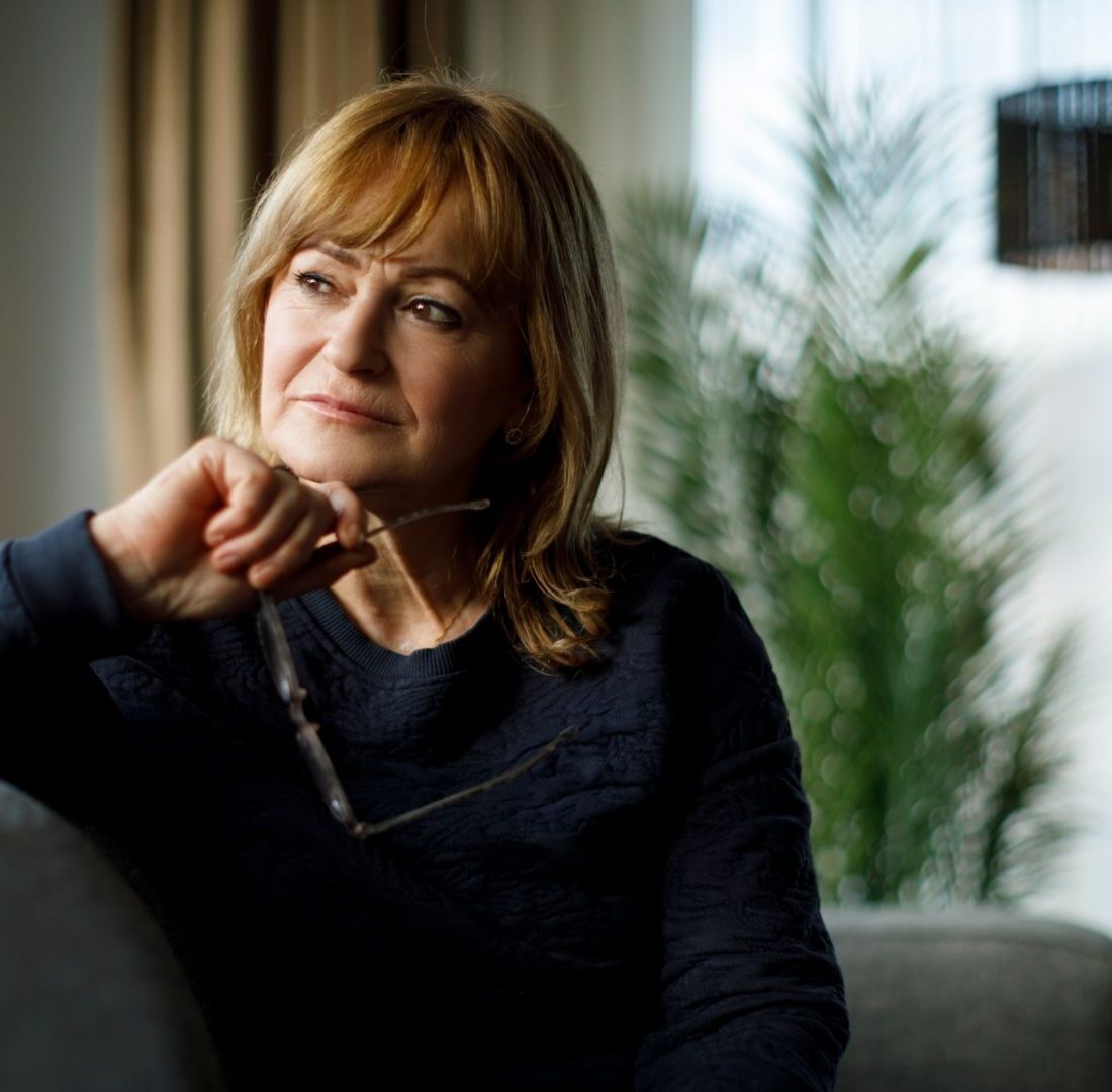 Vrouw met bril in hand zit op de bank en kijkt naar buiten