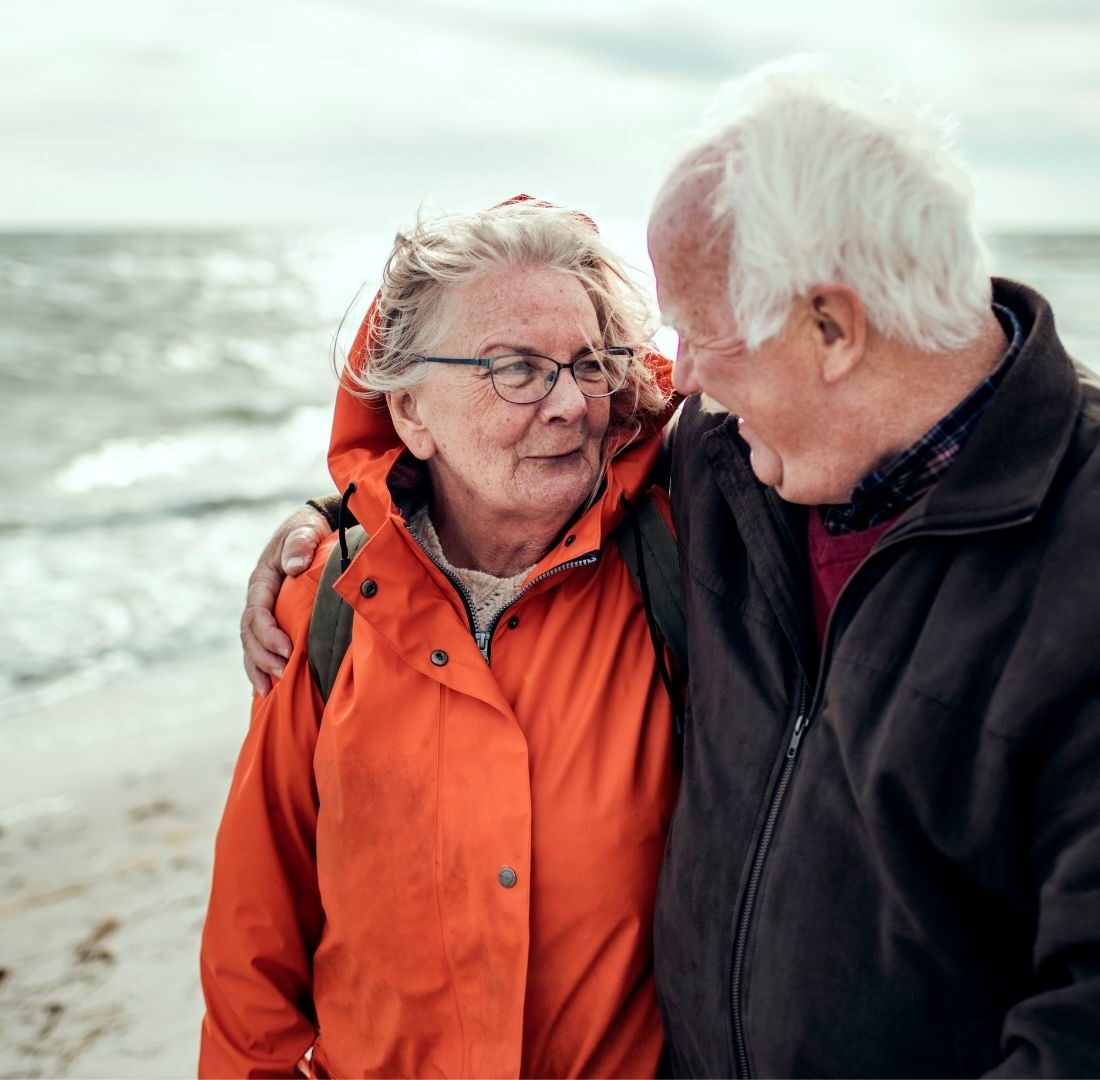 Een ouder echtpaar op het strand die verliefd naar elkaar kijken