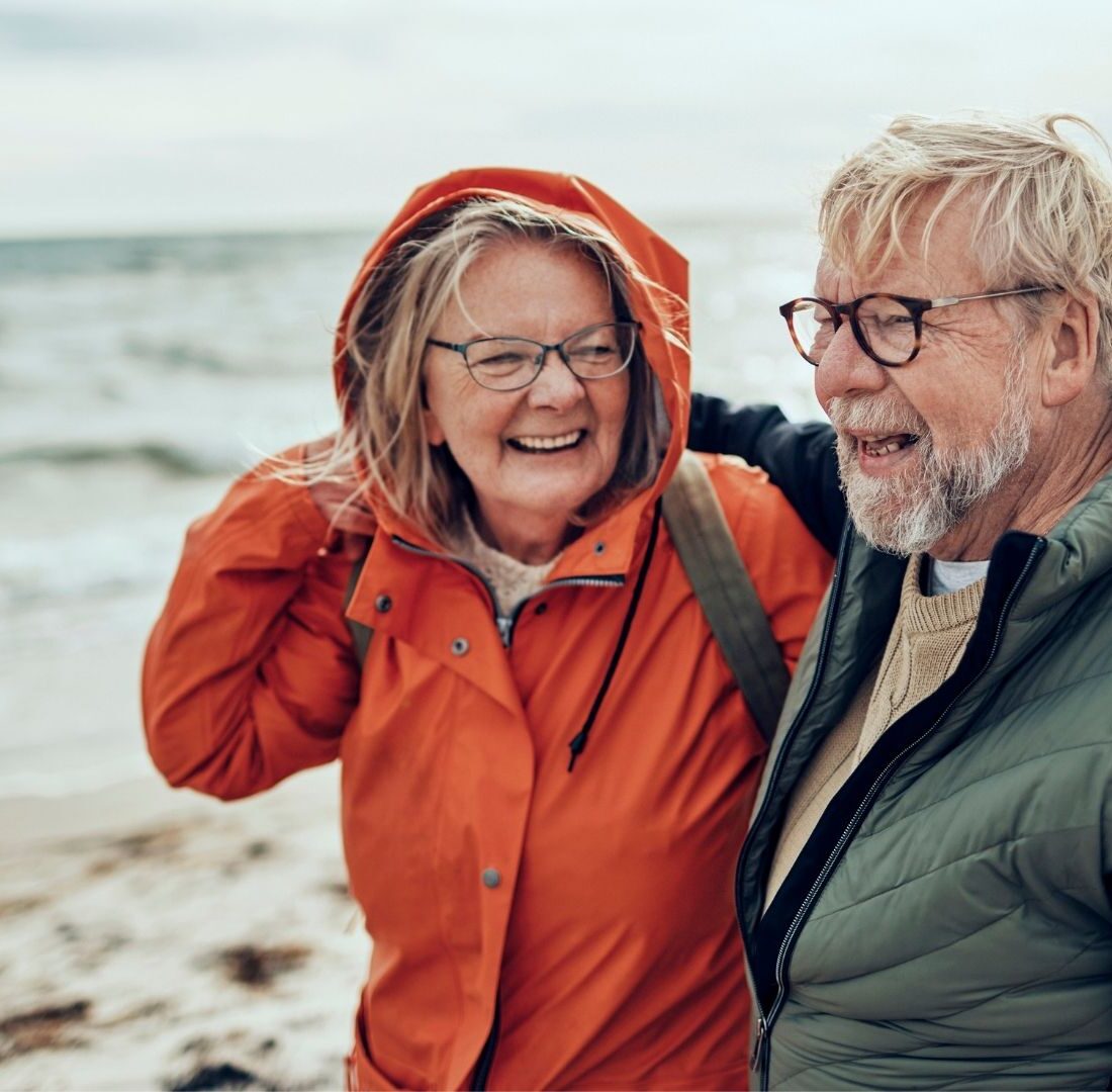 Een ouder echtpaar op het strand die blij naar elkaar kijken