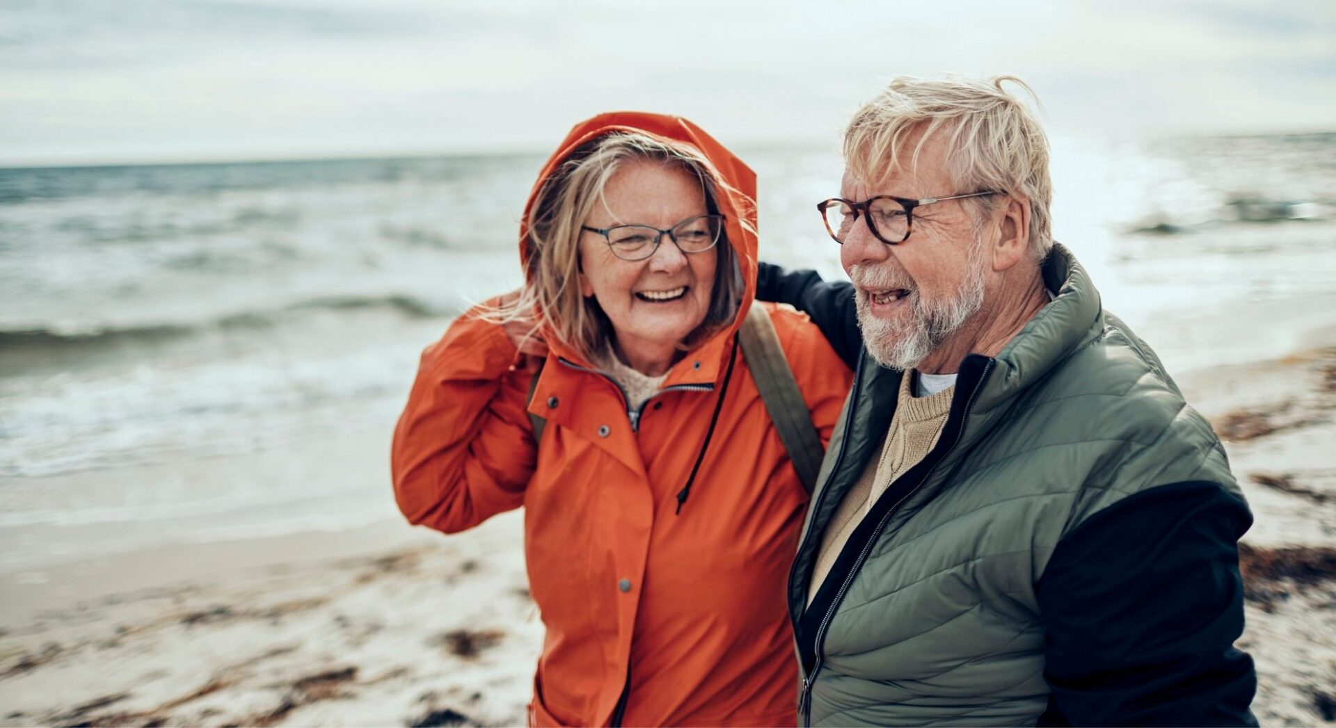 Een ouder echtpaar op het strand die blij naar elkaar kijken